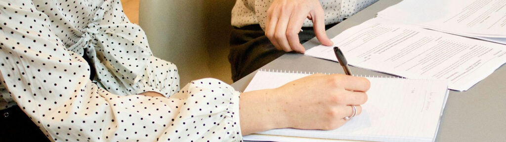 Person's hand holding a pen and writing on a piece of paper
